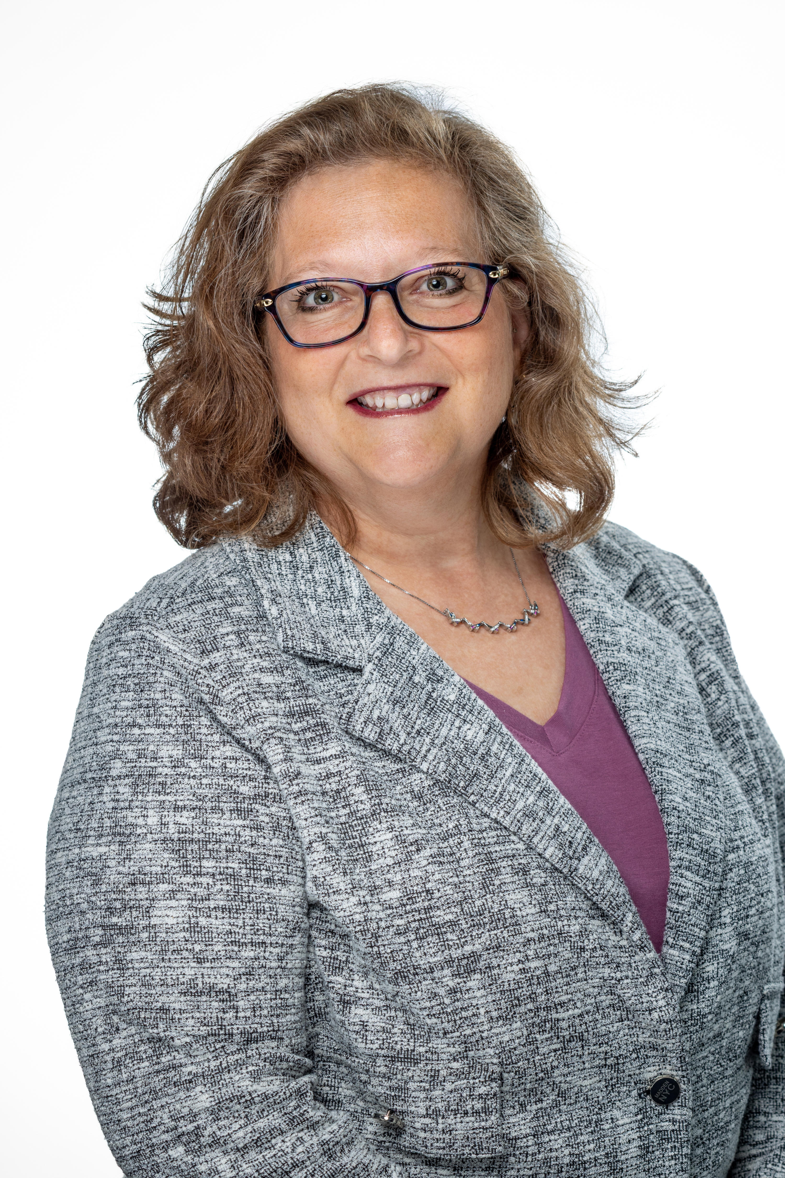 Portrait of Amy Greenberg, LCSW, MA.Ed, Assistant Dean for Student Affairs, smiling and wearing glasses, a gray blazer, and a purple top against a light background.